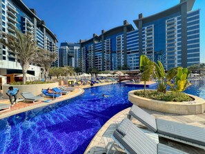 A swimming pool area with lounge chairs, palm trees, and high-rise buildings in the background.