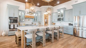 A modern kitchen with a central island, light blue cabinets, stainless steel appliances, and wooden accents.