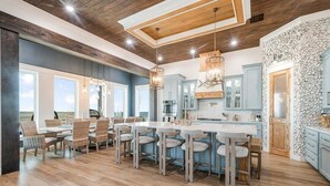 A spacious kitchen with a central island, wooden ceiling, and large windows.