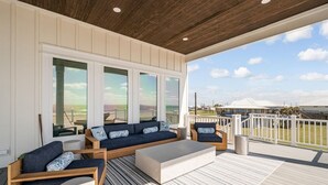 A covered outdoor seating area with a sofa, chairs, and a coffee table, overlooking a beach.