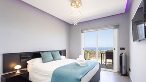 A modern bedroom with a large bed, a nightstand with a lamp, a TV mounted on the wall, and a balcony with a view. - Attico Boutique Apartment (San Eugenio)