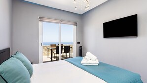 A modern hotel room with a large bed, a flat-screen TV, a view of the sea, and a balcony with outdoor seating. - Attico Boutique Apartment (San Eugenio)