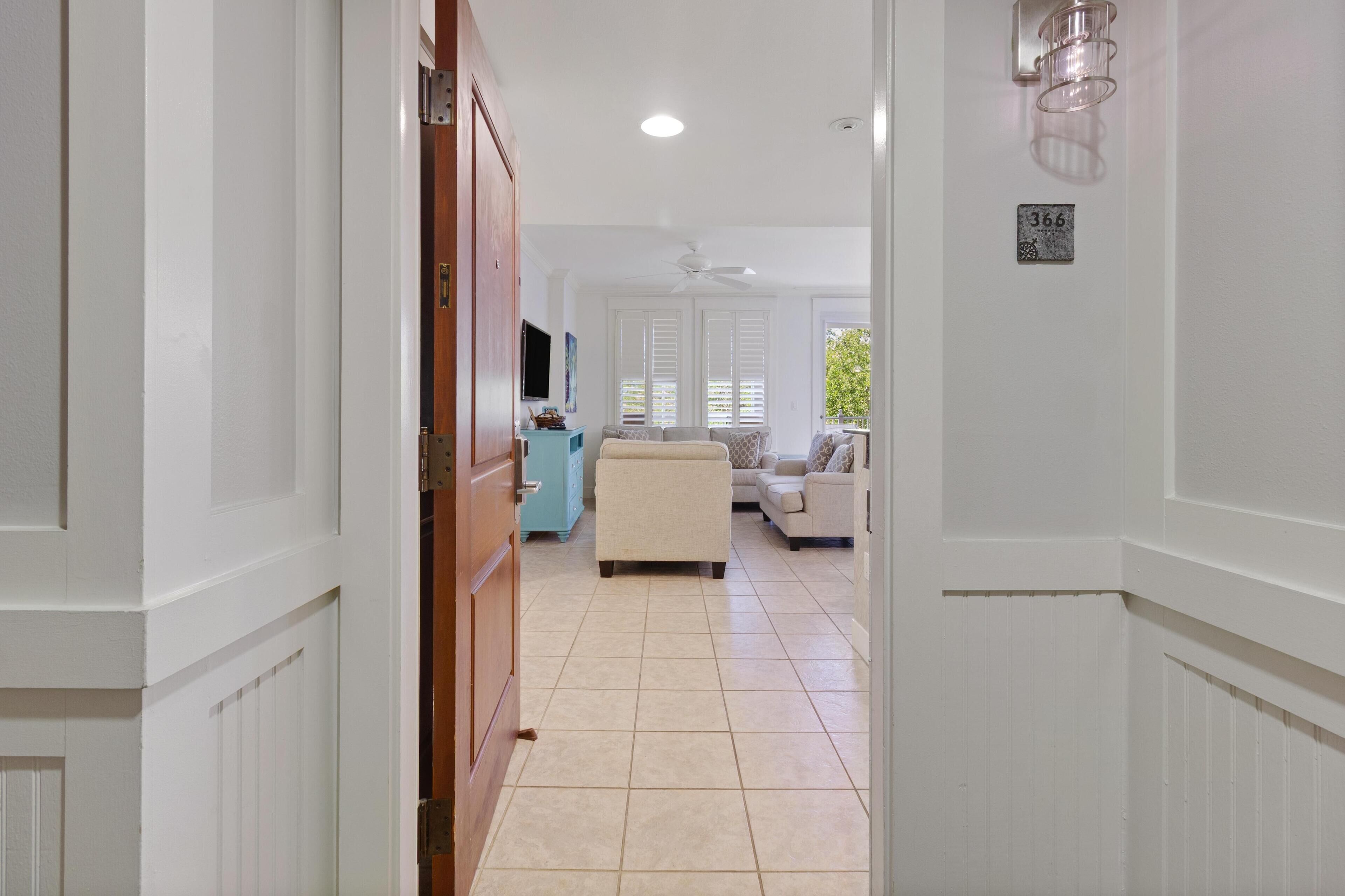Un couloir avec une porte en bois, un canapé beige et un téléviseur à l’arrière-plan.