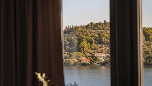A room with a view of a lake and a hill with buildings. There is a vase with flowers on a table. - Hotel Kali (Kali)
