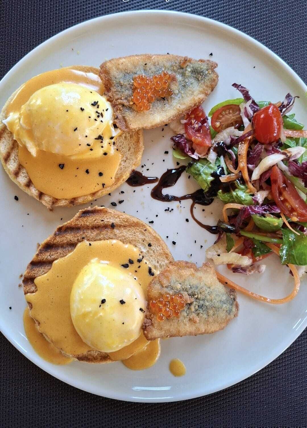 A plate with eggs benedict, caviar, and a side salad.