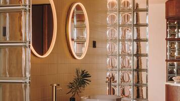 Ein modernes Badezimmer mit zwei Waschbecken, einem großen Spiegel und einer Glastrennwand.