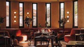 A restaurant interior with multiple seating areas, including tables and sofas, and large windows providing views of the outside.