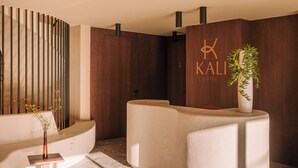 A modern hotel lobby with a reception desk, a seating area, and a wooden wall with the hotel name. - Hotel Kali (Kali)