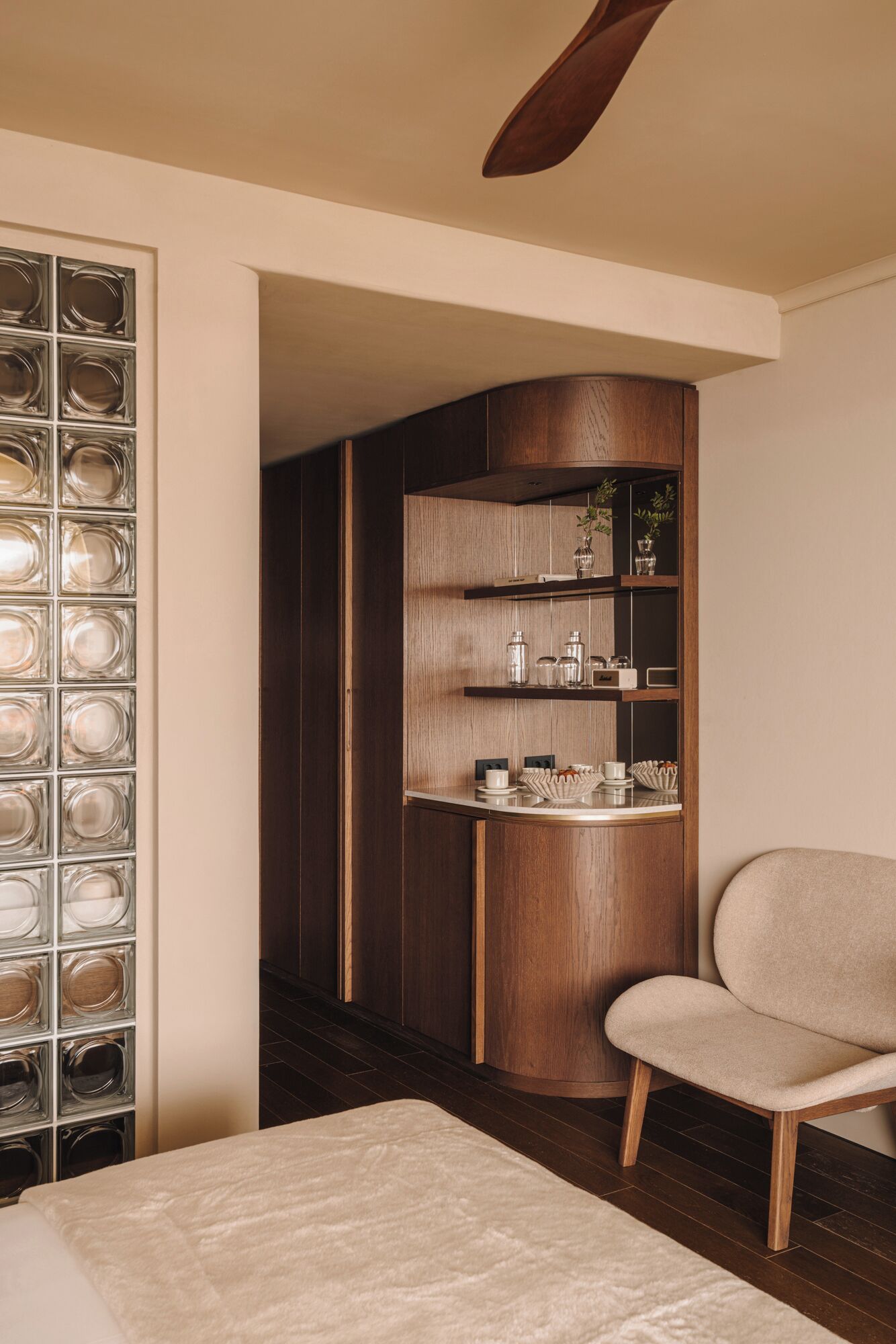 A modern bedroom with a wooden cabinet, a chair, and a glass block wall.