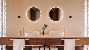 Un baño moderno con dos lavamanos, un espejo central y una planta decorativa.