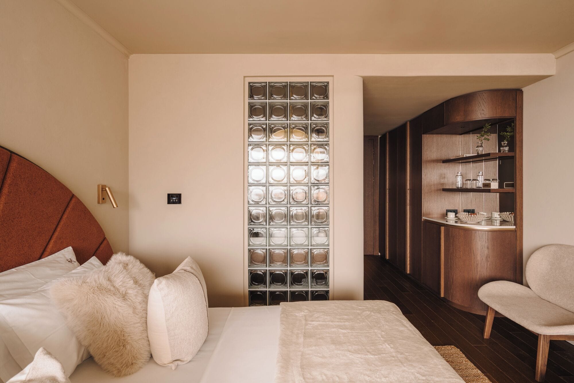 Ein Schlafzimmer mit einem Bett, einem Sessel, einer Holzschrank mit Regalen und einer Wand aus Glasbausteinen.