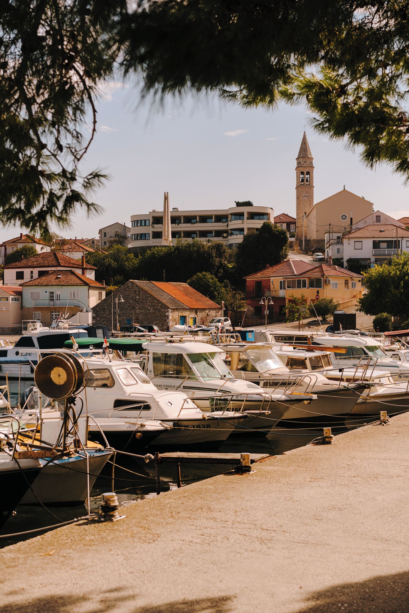 A marina with several boats docked, a prominent clock tower, and buildings with traditional architecture in the background.