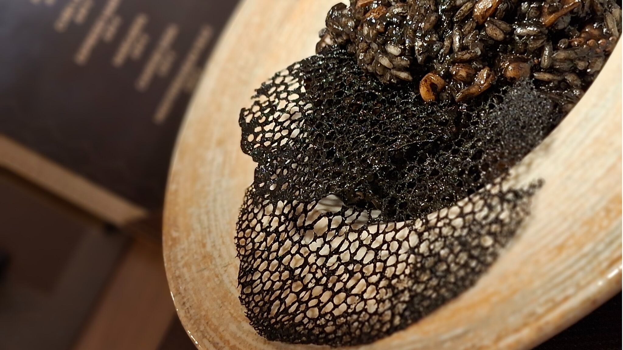Un gros plan d’un bol contenant un aliment à la texture particulière, peut-être un type de champignon, avec une structure sombre rappelant un réseau.