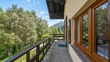 A balcony with a wooden railing, a blue chair, and a view of a forested area with mountains in the distance.