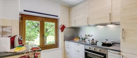 Una cocina moderna con armarios blancos, horno empotrado y ventana con vistas a zonas verdes.
