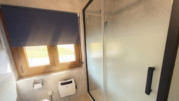 Un baño con ducha, inodoro, toallero y ventana con persiana.