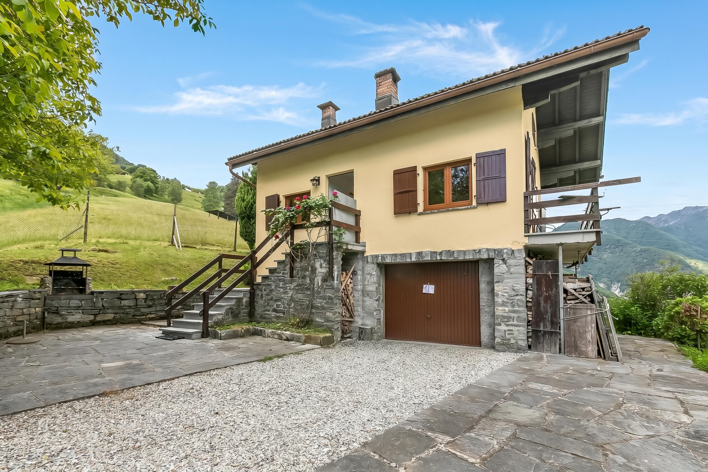 A two-story house with a stone staircase, a wooden deck, and a view of the surrounding hills.