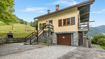 A two-story house with a stone staircase, a wooden deck, and a view of the surrounding hills.