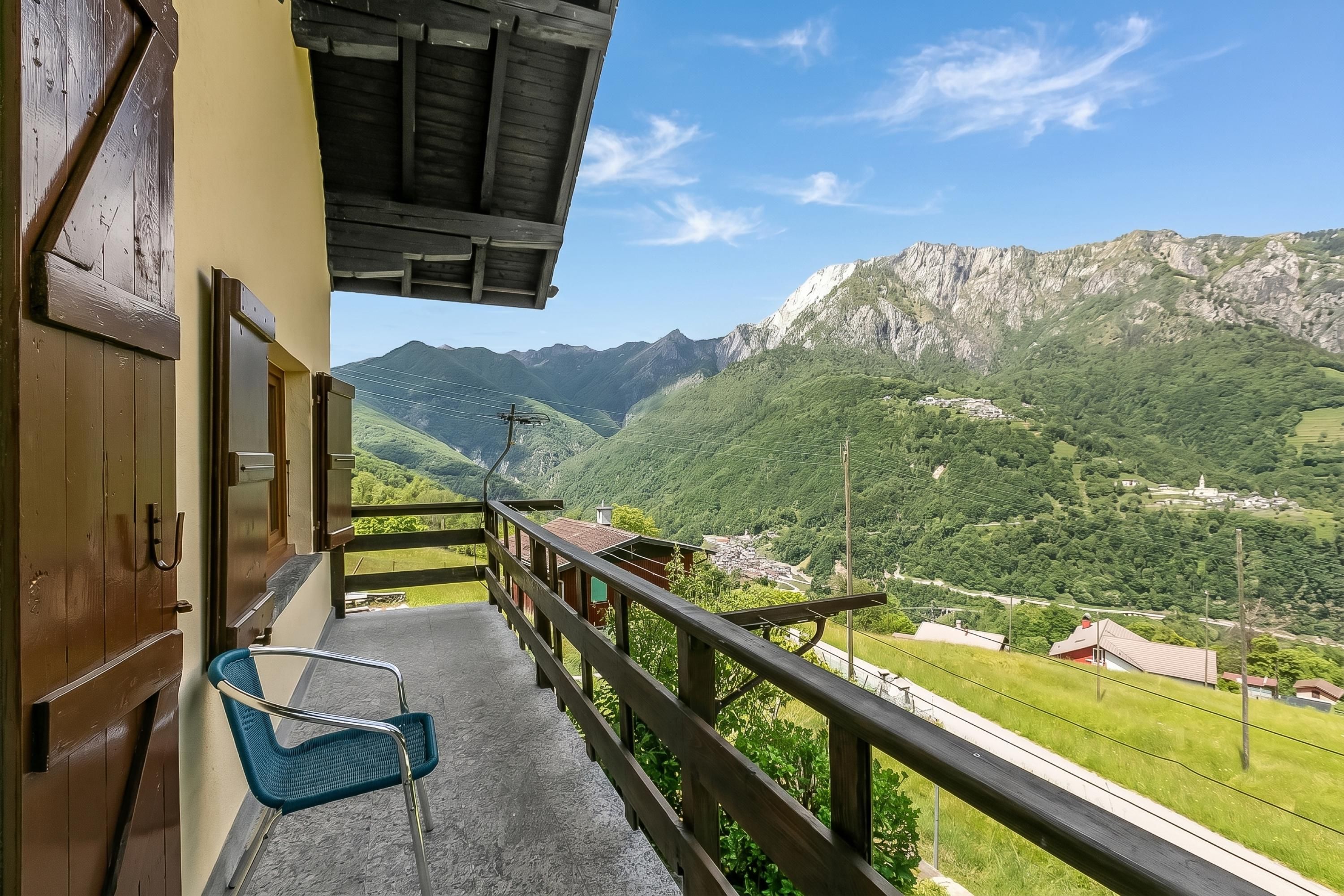 A balcony with a view of mountains, a chair, and a wooden railing.