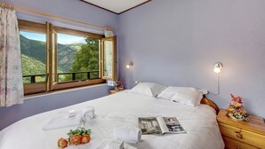A bedroom with a large bed, a window with a view of green hills, a bedside table with a lamp, and a nightstand with a flower arrangement. - Casa Clelia Centovalli With Private Garden (Centovalli)