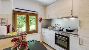 A modern kitchen with white cabinets, a built-in oven, and a window with a view of greenery. - Casa Clelia Centovalli With Private Garden (Centovalli)