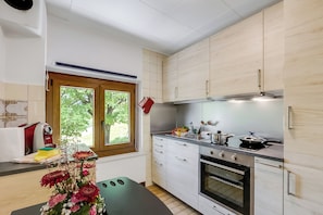 A modern kitchen with white cabinets, a built-in oven, and a window with a view of greenery. - Casa Clelia Centovalli (Centovalli)
