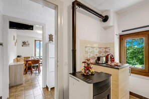 A kitchen with a stove, a window with a view, a dining area with a table and chairs, and a hallway leading to another room. - Casa Clelia Centovalli With Private Garden (Centovalli)