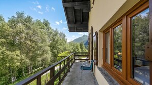 A balcony with a wooden railing, a blue chair, and a view of a forested area with mountains in the distance. - Casa Clelia Centovalli With Private Garden (Centovalli)