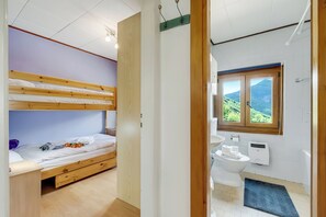 A room with a bunk bed, a wooden door, a bathroom with a toilet, a sink, and a window with a view of greenery. - Casa Clelia Centovalli With Private Garden (Centovalli)