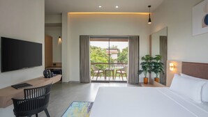 A modern hotel room with a large bed, a desk with a flat-screen TV, a coffee maker, and a balcony with a view of greenery. - Gir Aatithya Clarks Inn  (Talala)