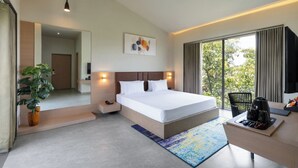 A modern hotel room with a large bed, bedside tables, a desk with a chair, a potted plant, and a view of greenery through the window. - Gir Aatithya Clarks Inn  (Talala)