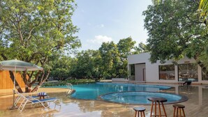 A swimming pool with lounge chairs and a bar area, surrounded by trees and a modern building. - Gir Aatithya Clarks Inn  (Talala)