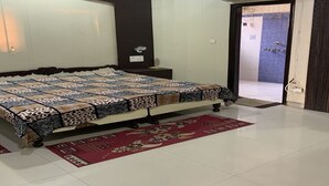 A bedroom with a large bed, a nightstand, a red rug, and a bathroom visible through an open door. - Modern Apartment with Kitchen & Wi-Fi – Perfect for Work & Relaxation (Sahibzada Ajit Singh Nagar)