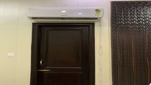 A wall-mounted air conditioner above a dark wooden door with a textured panel to the right. - Modern Apartment with Kitchen & Wi-Fi – Perfect for Work & Relaxation (Sahibzada Ajit Singh Nagar)