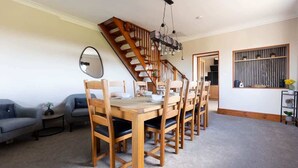 Un comedor con una mesa y sillas de madera, una escalera, un espejo y una mesita auxiliar con una planta.