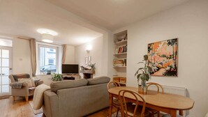 A living room with a sofa, TV, and bookshelves. - Charming Ulverston Cottage with Garden & Views (Westmorland and Furness)