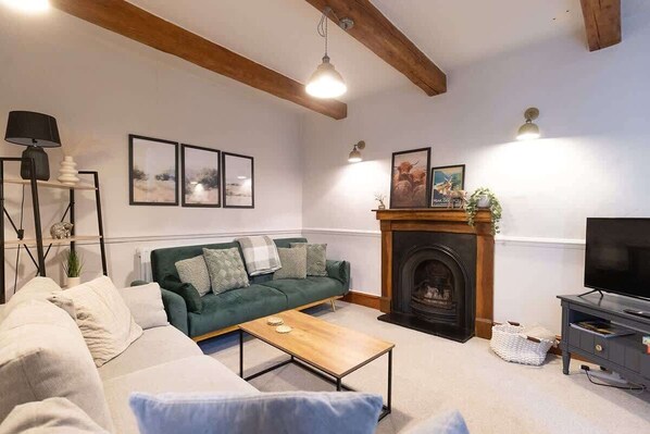 A living room with a green sofa, a wooden coffee table, a fireplace, and a television.