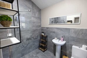 A modern bathroom with grey tiles, a white sink, a mirror, and a shower area.