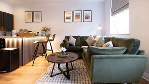 Un salon moderne avec un canapé vert, une table basse et un coin cuisine doté d’un comptoir et de chaises.