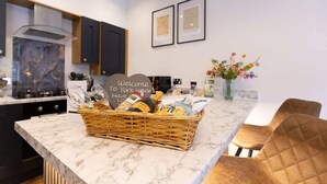 Une cuisine dotée d’un plan de travail en marbre, d’un panier en osier rempli de produits alimentaires et d’une pancarte de bienvenue.