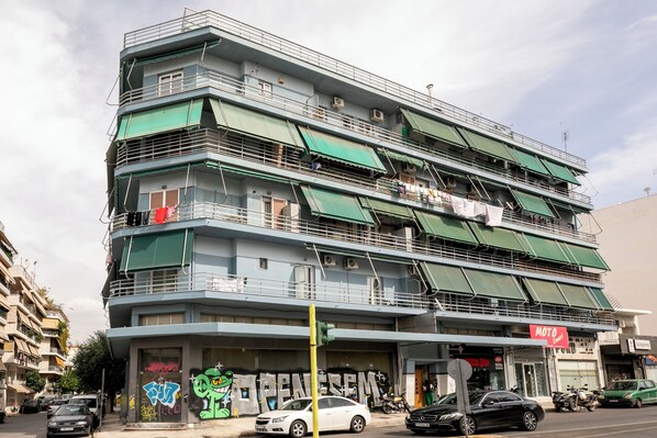 Ein mehrstöckiges Gebäude mit Balkonen, einem sichtbaren Schaufenster und parkenden Autos.