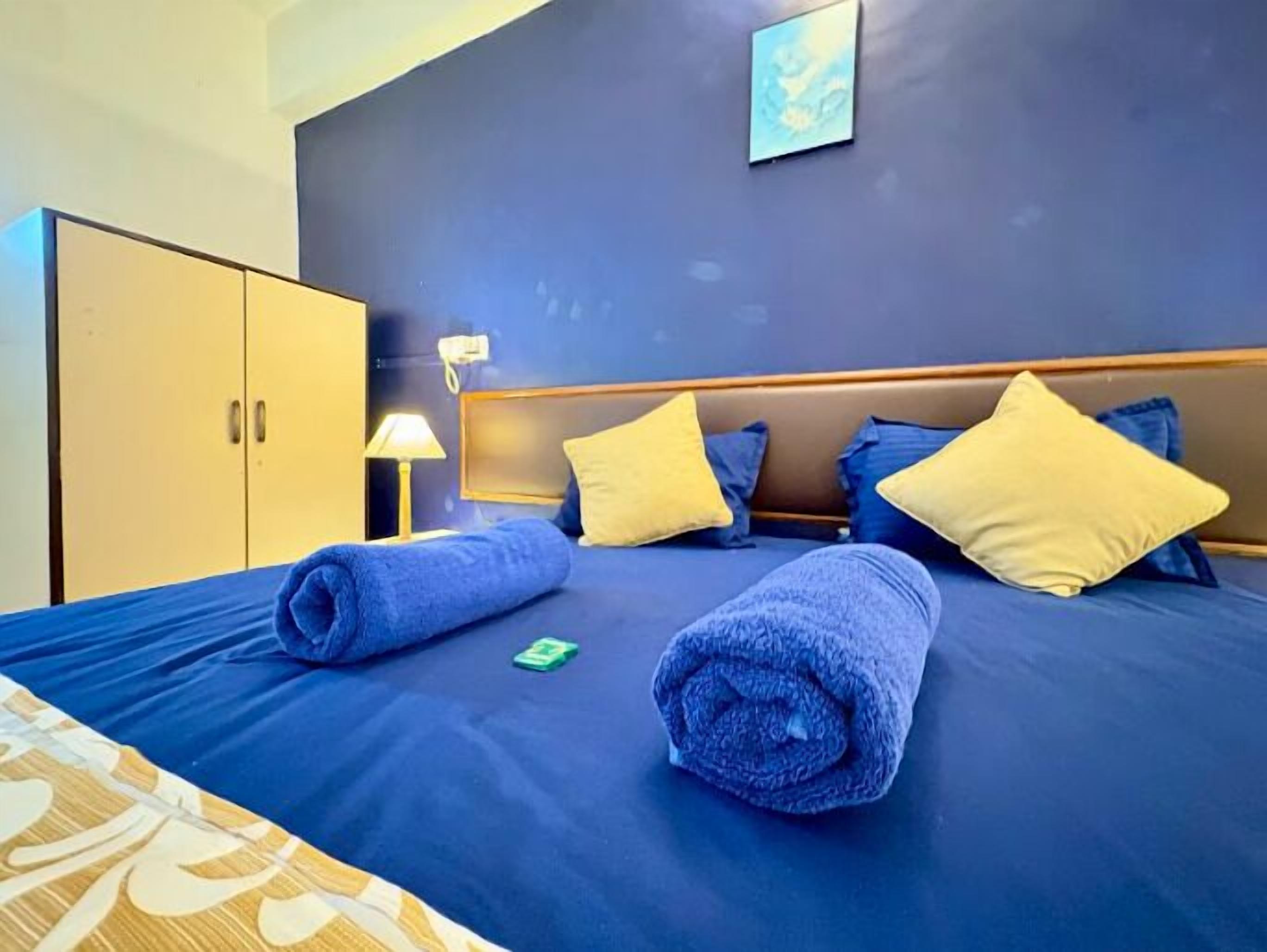 A hotel room with a bed, pillows, a nightstand, a lamp, and a wardrobe.
