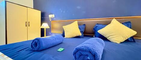 A hotel room with a bed, pillows, a nightstand, a lamp, and a wardrobe.