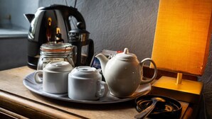 Una bandeja con un hervidor de agua, dos tazas, una prensa francesa y una lámpara pequeña sobre una mesa de madera.