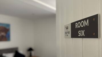 Una señal que indica 'ROOM SIX' en una habitación de hotel con una cama, almohadas y una mesita de noche.
