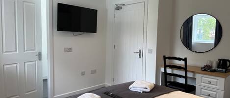 Une chambre d’hôtel comprenant un lit, un téléviseur fixé au mur, un miroir, un bureau avec une chaise et une fenêtre.
