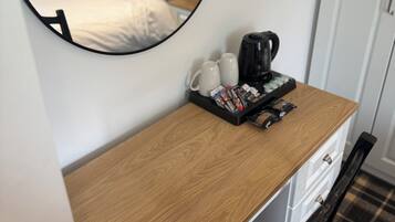 A hotel room with a wooden desk, a coffee maker, and a tray of magazines.