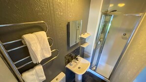 Un baño moderno con ducha de vidrio, lavabo blanco y un perchero para toallas.