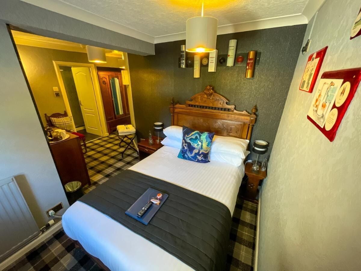 Et hotelværelse med en stor seng, et træhovedgærde, et skakternet gulv, et skrivebord med stol og en lampe.