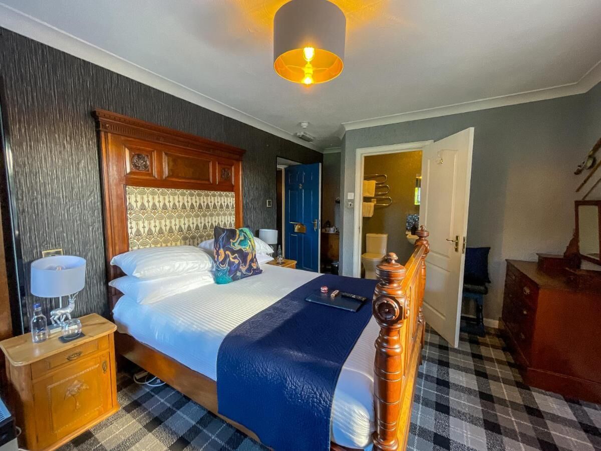 Ein Hotelzimmer mit einem großen Bett, einem hölzernen Kopfteil, einem Nachttisch mit einer Lampe und einem karierten Boden.